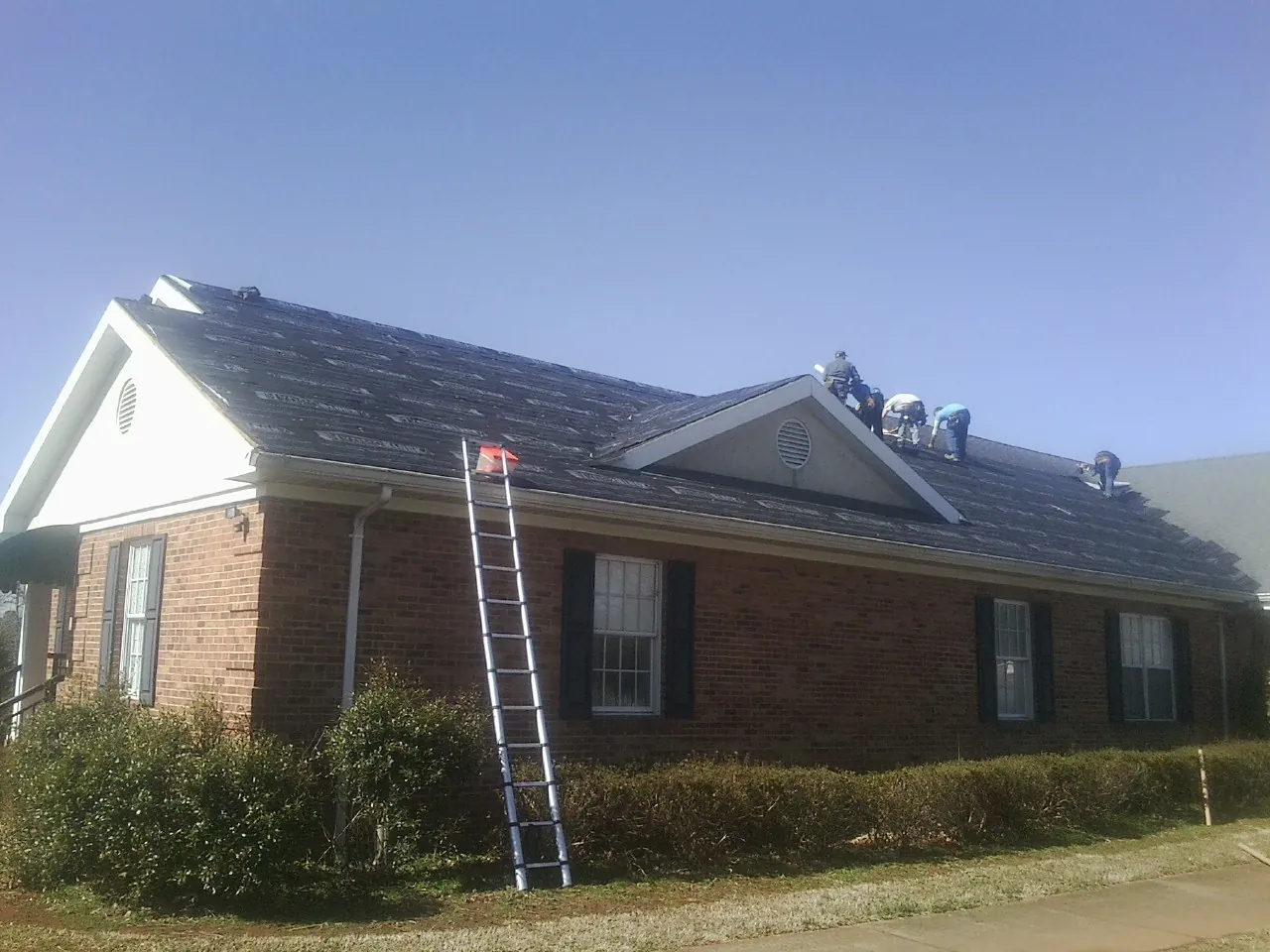 Crew tearing shingles off a brick ranch roof with a ladder set — Emergency Roof Repair work by our crew in New Carlisle