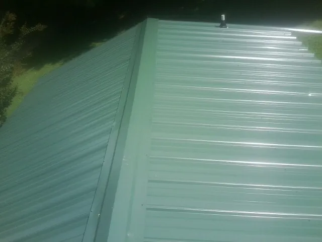 New green metal panels meeting at the ridge of a roof — Flat Roof Repair work by our crew in New Carlisle