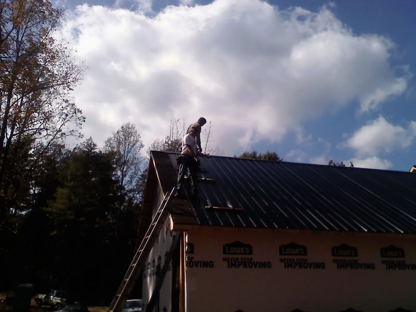 Roofer fastening dark metal panels high against a cloudy sky in New Carlisle